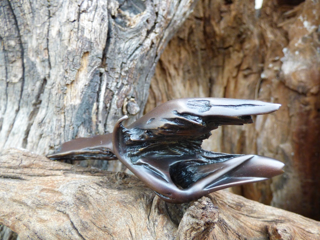 Front view of miniature bronze sculpture titled Gotcha!, in bronze, against a background of weathered wood.