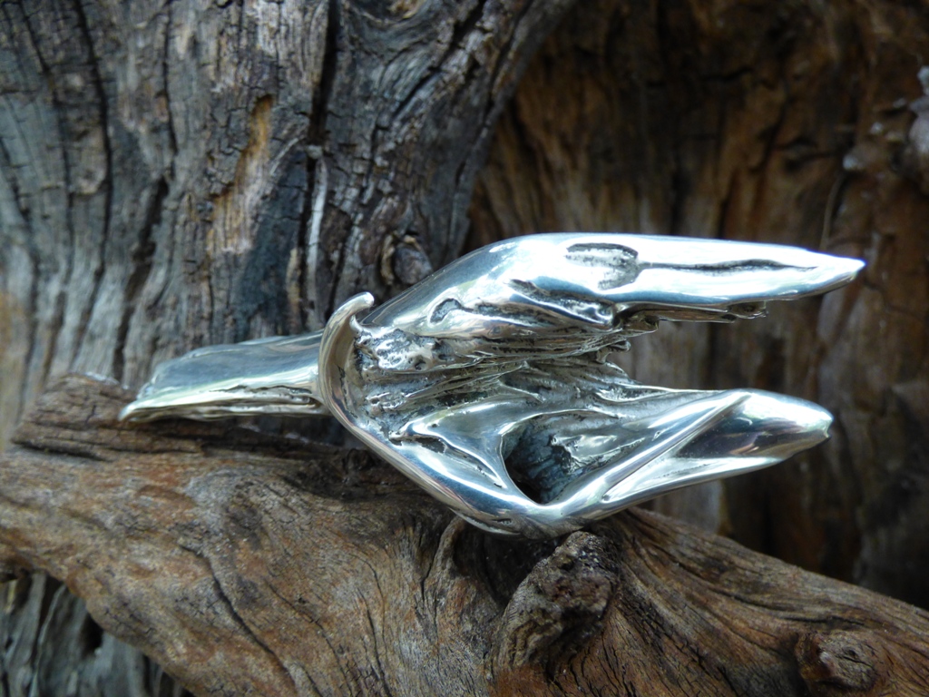 Front view of miniature sterling silver sculpture titled Gotcha!, against a background of weathered wood.